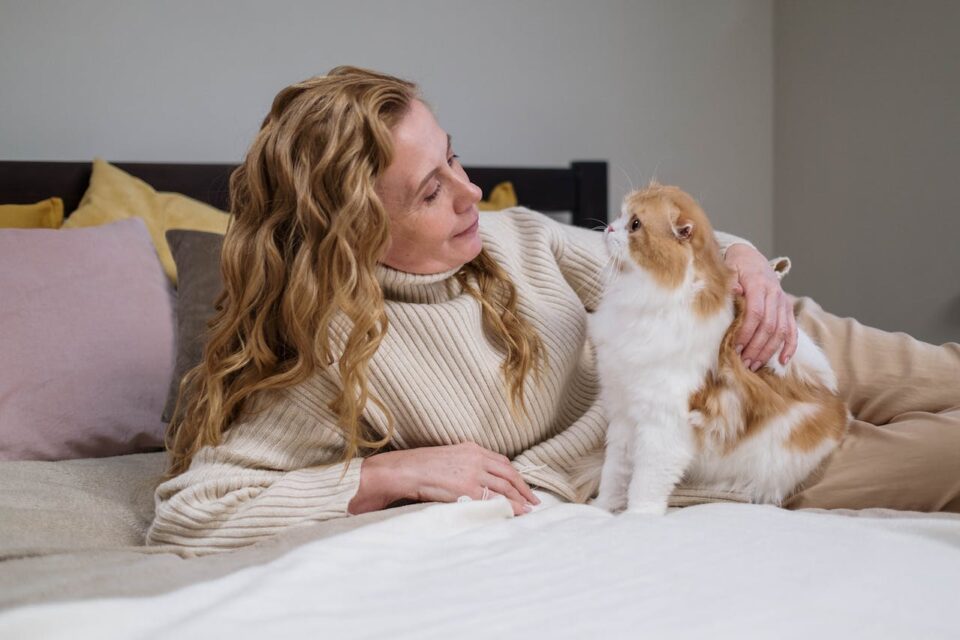 an owner laying on a bed next to her cat